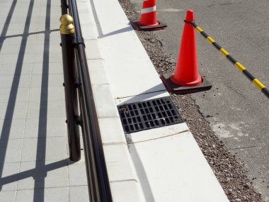 Turuncu trafik konileri metal drenaj ızgarasının yanında duruyor.