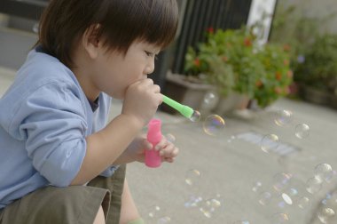Parkta sabun köpüğü üfleyen Asyalı çocuk