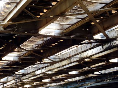 Endüstriyel metal kirişlerden ve yıpranmış çatılardan güneş ışığı akıyor.