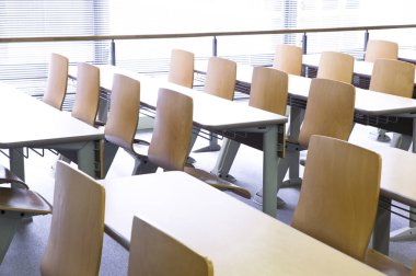 Okuldaki boş sınıfın içinde. Sıralar dolusu tahta masa ve sandalye.