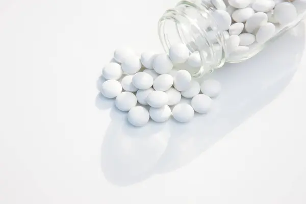 stock image white pills poured out glass jar on white background