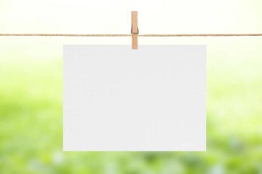 Elbise ipinde asılı boş bir kağıt parçası, bulanık yeşil yaz arkaplanı.