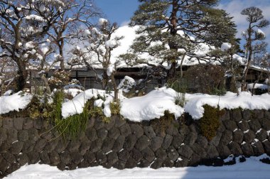Geleneksel Japon evi karla kaplı taş duvarla çevrili.