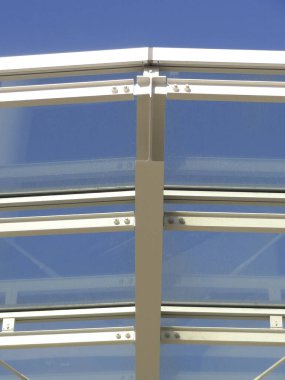 Mavi gökyüzüne karşı güneş ışığını yansıtan modern cam çatı yapısı