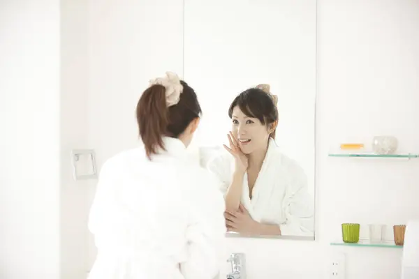 young Japanese woman looking in mirror at bathroom