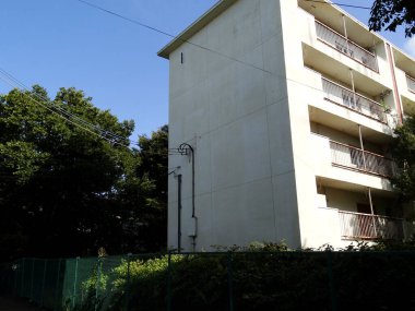 Yeşil ağaçların ve çitlerin yanındaki güneşli apartmanda.