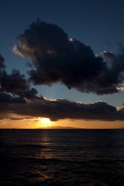 Okyanusun üzerinde dramatik bulutlarla portakal rengi günbatımı