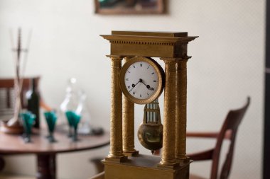 Ahşap mobilyaların yanındaki kolonların arasında duran antik altın saat.