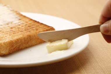 Butter being spread on a slice of freshly toasted bread on a wooden table clipart