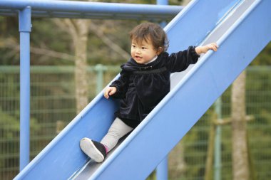 Küçük tatlı Asyalı kız çocuk oyun parkında kaydırak oynuyor.