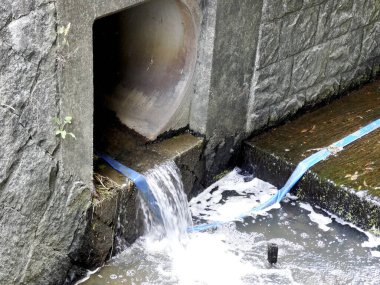 Beton drenaj borusundan ıslak kaldırım yüzeyine akan su.