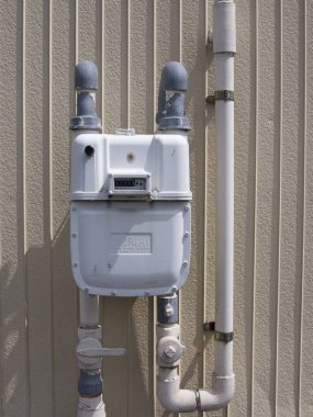 Borularla bej duvara bağlı beyaz gaz sayacı