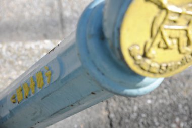 Kapalı çekimde açık havada mavi metal çubuk ve sarı kabartmalı detaylar görülüyor.