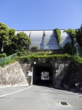 Güneşli bir gün yeşil yamacın altındaki tünel girişini gösteriyor.