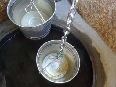 Taş suyun üzerinde asılı metal kovalar.