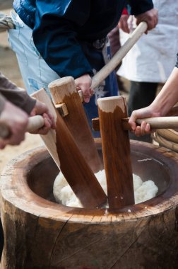 İnsanlar dışarıda tahta sopalarla pirinç dövüyorlar.