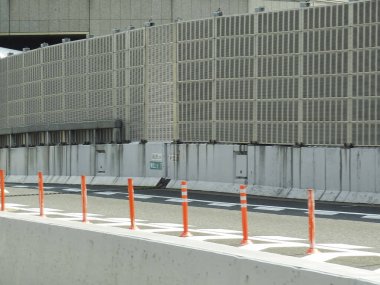 Uzun beton ses bariyerleri ve turuncu sütunların yanında boş otoyol şeridi