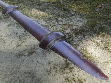 Paslı metal mızrak dışarıda kumlu zeminde çapraz yatıyor.