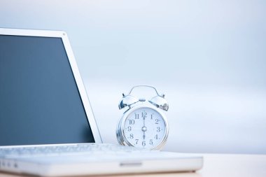 Işık arkaplanındaki dizüstü bilgisayar ve alarm saatinin yakın görüntüsü    