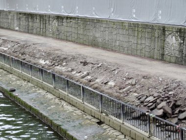 Kentsel nehir inşaatı enkazı yanında yıkılan beton set görünür.