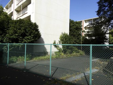 Yüksek apartmanların yanında güneşli, boş çitli bir alan.