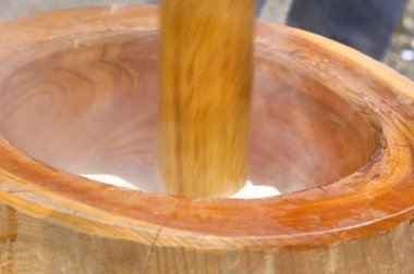 Dışarıdaki ahşap havan içinde yapışkan pirinç dövüyor.