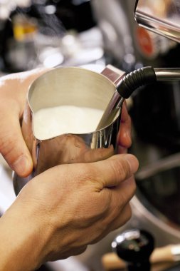Kahve makinesi kullanarak kapuçino köpüğüne süt hazırlayan barmen. 