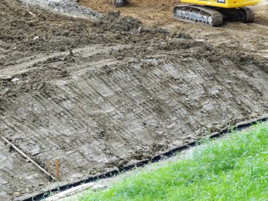 İnşaat ekipmanları kullanılarak çimenli bölgenin yakınındaki toprak yüzeyinin derecelendirilmesi