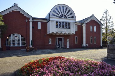 Beyaz sütunlar ve çiçek açan çiçeklerden oluşan kırmızı tuğla bina.