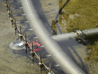 Kavisli metal boru sistemi açık havada sığ sulara gömülmüş.