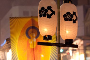 Aydınlatılmış Japon fenerleri renkli festival afişlerinin yanında asılı.