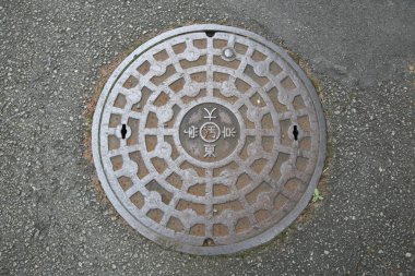 Yuvarlak drenaj kapağı ve kentsel alanın yakınındaki beton kaldırımda karışık desenler var.