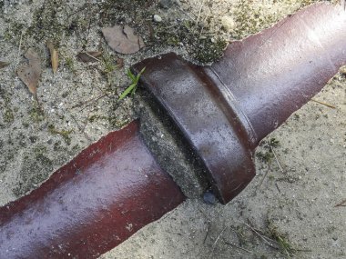 Kırık kırmızı boru kumlu zemin yüzeyinde yatıyor.