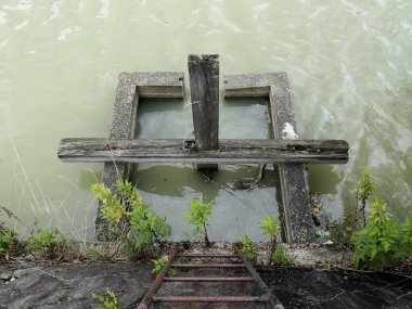 Betondan yapılmış eski, küçük bir baraj ya da iskele kapısı bulanık bir su kütlesinin kenarında oturur..