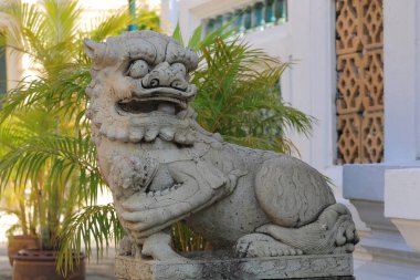 Yeşil bitkilerin yanında taş aslan heykeli