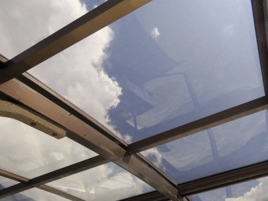 Mavi gökyüzünü ve kabarık beyaz bulutları gösteren cam tavan