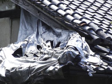 Hasarlı çatı gümüş muşamba ve kırık fayanslarla kaplı.