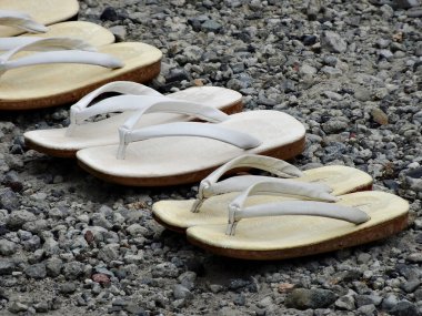 Yazın güneşli bir havada kumsalda çakıl taşı yüzeyine dizilmiş terlikler.