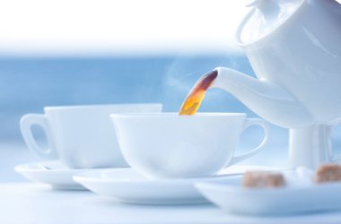 Beyaz bardakta bir masaya çay dökülüyor. 