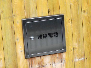 Siyah metal panel Japon yazılarını sarı tahta duvarda sergiliyor.