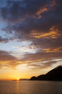 Gün batımında gökyüzü ve bulutların arasında güneş olan sakin bir deniz. Meditasyon okyanusu ve gökyüzü arka planı. Huzurlu deniz manzarası 