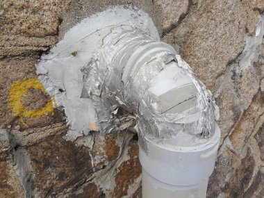 Hasarlı beyaz boru, taş duvara sert yama kullanarak mühürlendi.