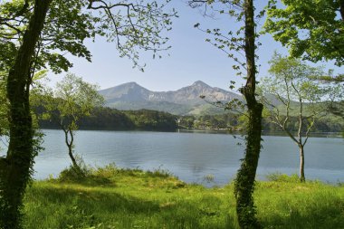 Gölü, yeşil ağaçları ve arka planda dağları olan güzel bir manzara.           