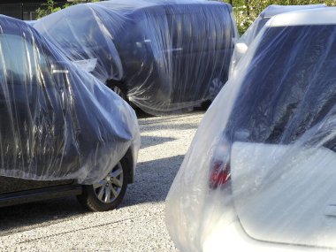 Çakıl taşı yüzeyine park edilmiş plastik ambalajlarla kaplı arabalar.