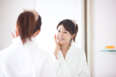 Genç Japon kadın banyoda aynaya bakıyor.
