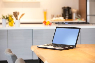 Mutfaktaki ahşap masada boş ekranlı dizüstü bilgisayar.