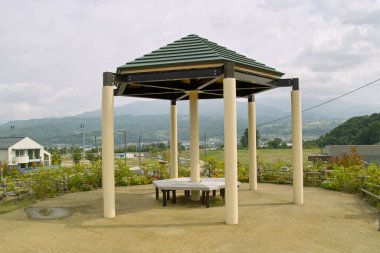 Boş çardak yapısı bulutlu gökyüzünün altında yeşil tepelerin arasında duruyor.