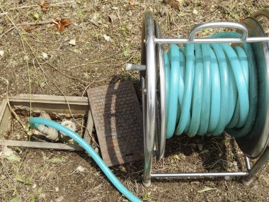 Metal makaranın etrafına sarılmış yeşil bahçe hortumu.