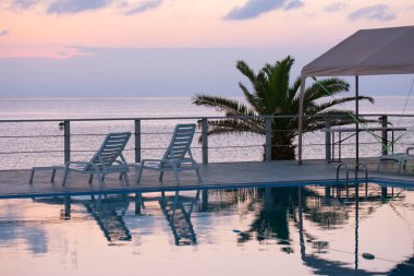 Deniz manzarası ve beyaz ahşap sandalyeli boş yüzme havuzu.