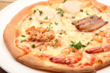 Lezzetli pizza, et ve otlarla kaplı. Sıradan bir lokantada beyaz bir tabakta servis ediliyor.